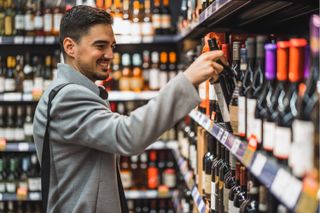 A man picking up a bottle of wine from a shelf in a shop