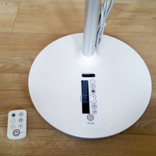 The base of the white pedestal EcoAir Kinetic fan and remote control on a wooden floor