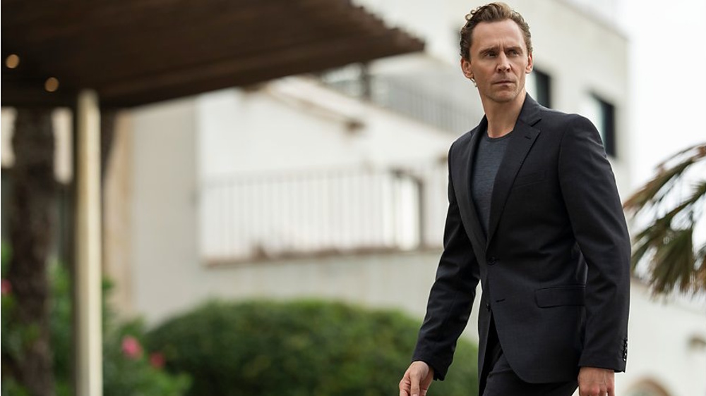 Tom Hiddleston as Jonathan Pine looking serious and dressed in a suave suit in a press image for The Night Manager Season 2.