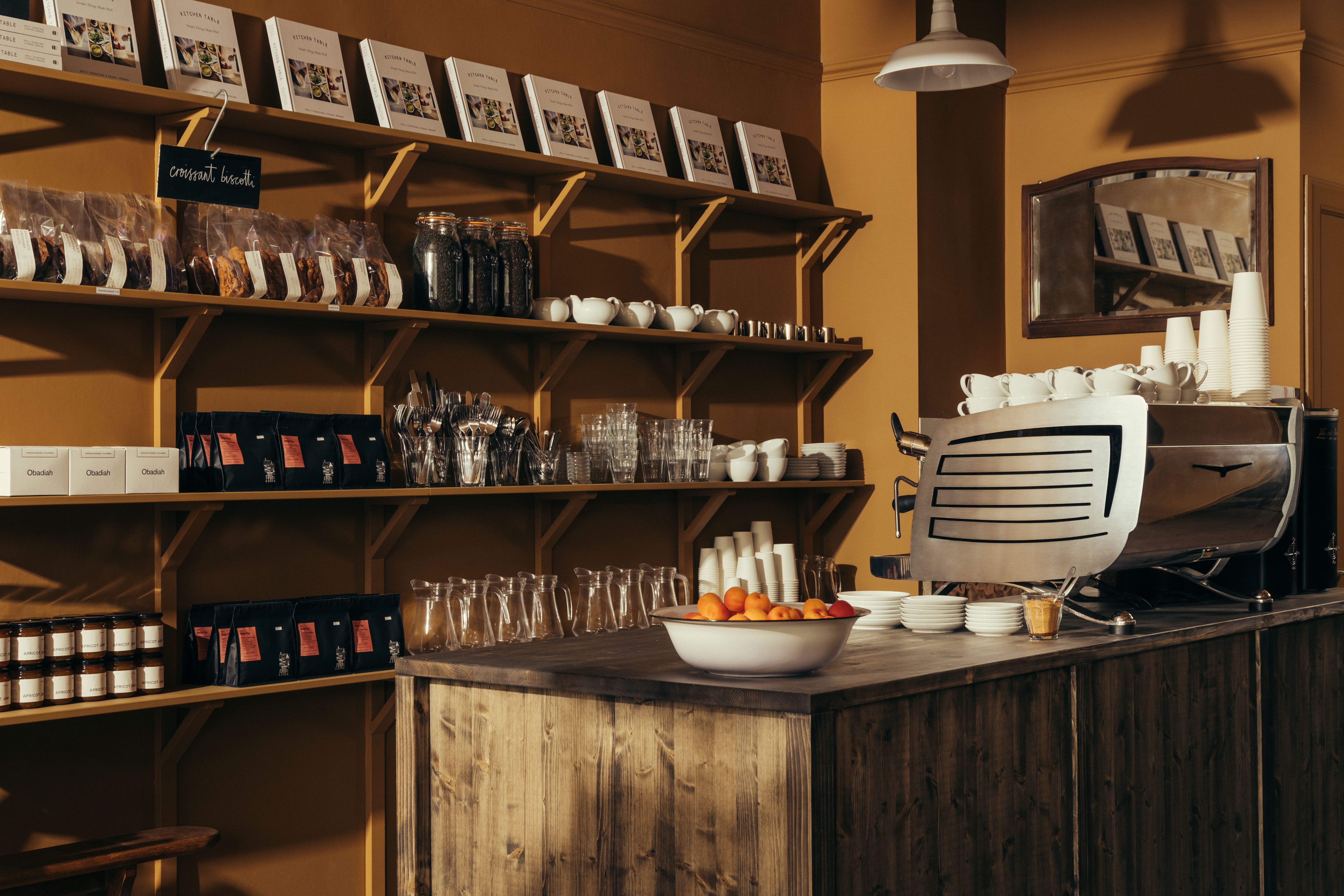 An ochre-painted cafe and bakery filled with wooden furnishings and industrial pendant lighting, along with lots of freshly baked goods, beautifully plated food, and coffee cups.