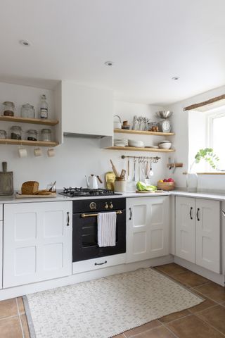 A small white farmhouse style kitchen with open shelving and stone floor tiles