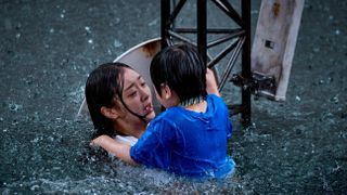 a woman holds her son as they hang onto a structure while floating in flood water