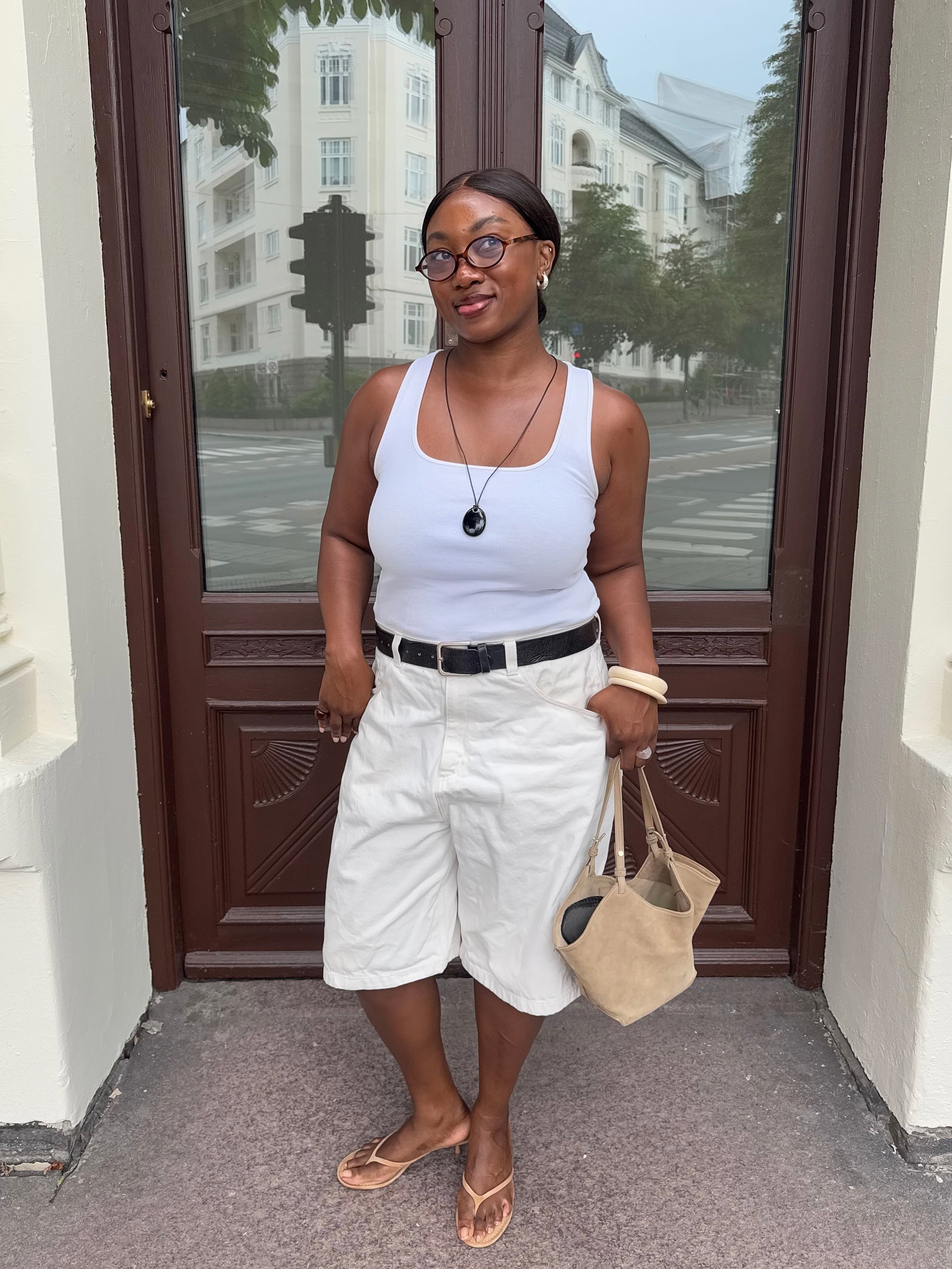Woman in a white top and Bermuda shorts with black and tan accessories.
