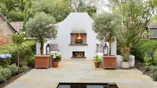Outdoor fireplace with olive trees in pots in mediterranean-style outdoor living area