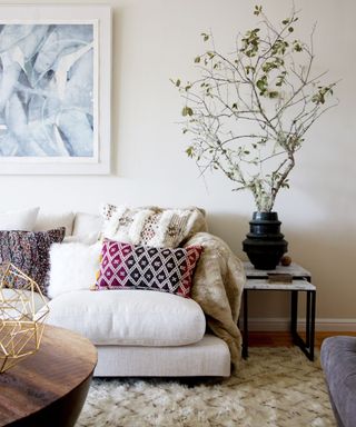 bohemian living room with neutral sofa and walls, house plant and layered pillows and rug
