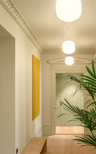 A hallway with a yellow painting and a sage green cabinet