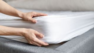 A pair of hands on a mattress, one hand on the top, the other holding the base, checking the mattress firmness and depth