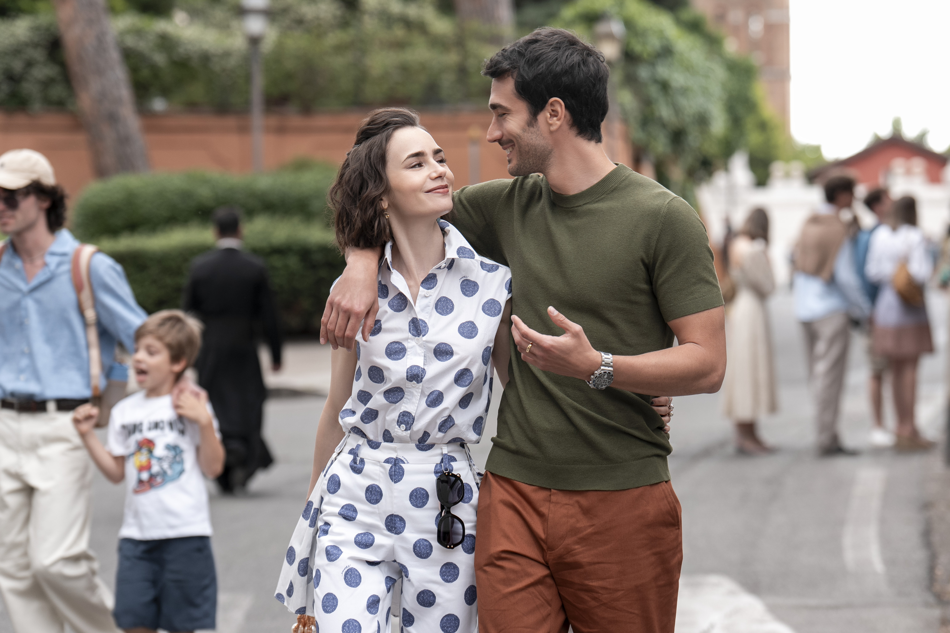 emily wearing a polka dot dress and marcello walking together through an italian city in emily in paris season 5