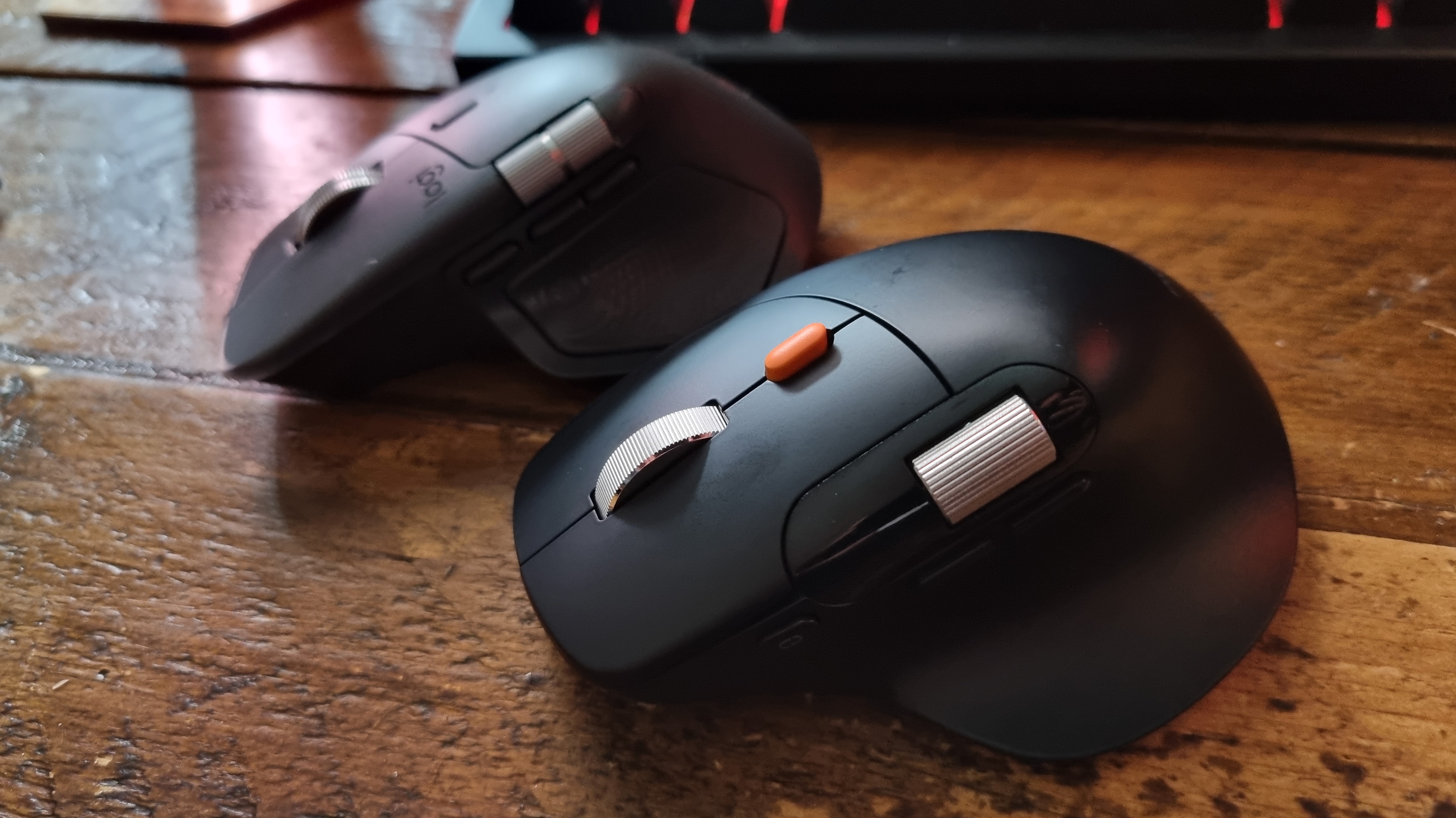 A ProtoArc EM25 ergonomic mouse in front of a Logitech MX Master 4 on a wooden desk