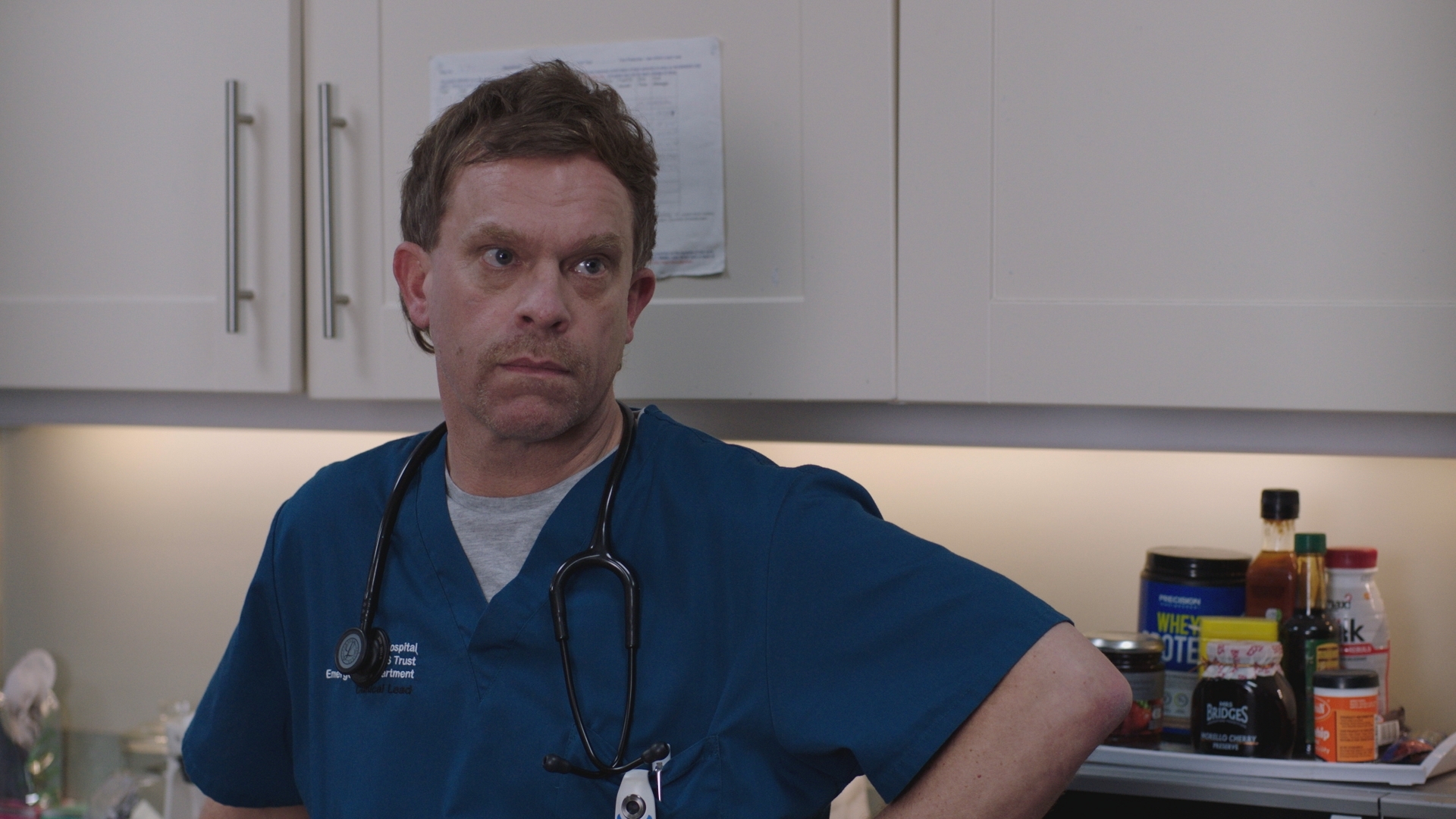 Dylan Keogh standing in the Holby ED staff room looking unimpressed in the sixth instalment of Casualty 12-parter Supply and Demand.