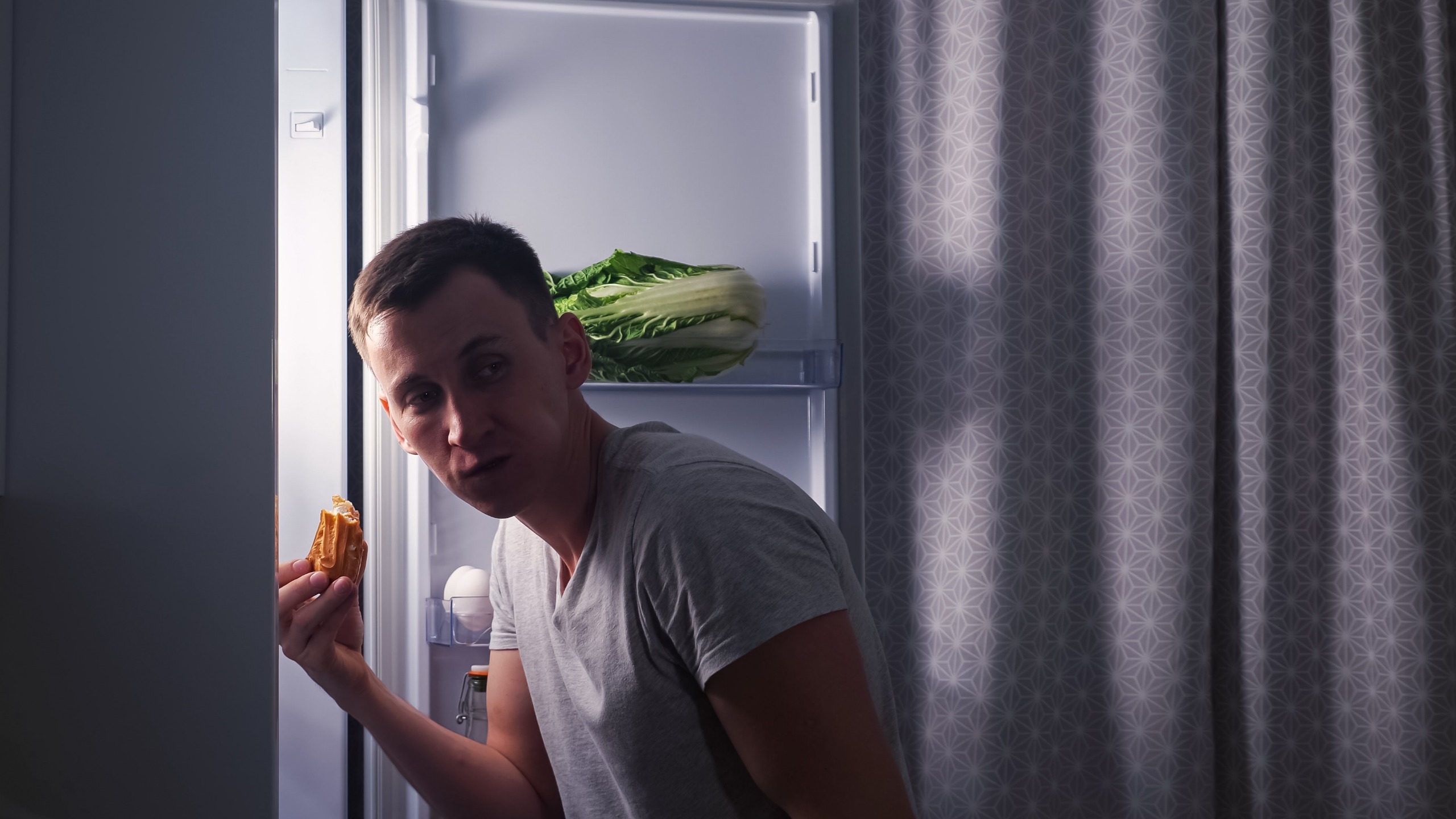 A man hides in the fridge whilst eating an eclair
