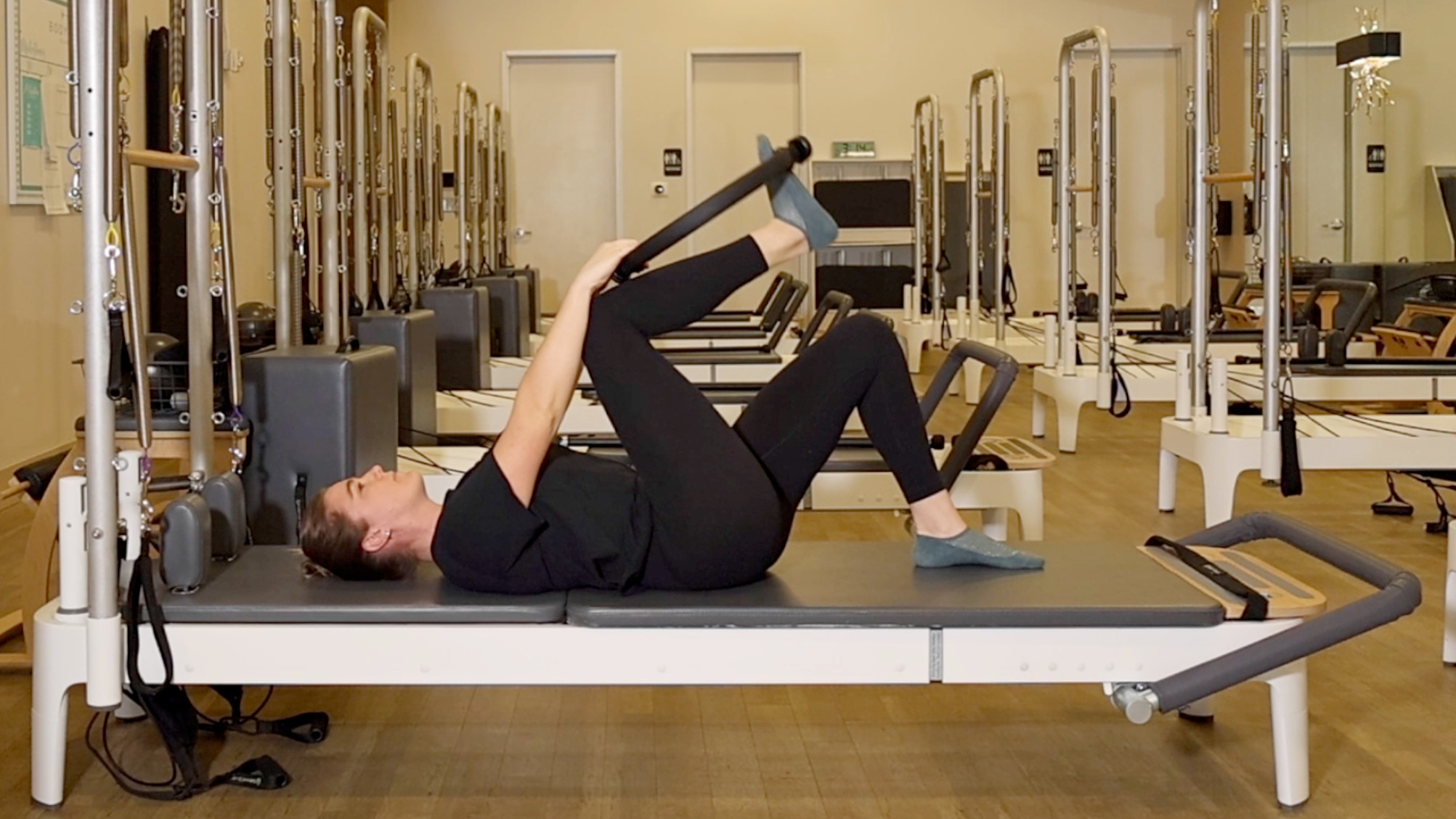 Woman demonstrating a Pilates exercise on the carriage of a Pilates reformer machine