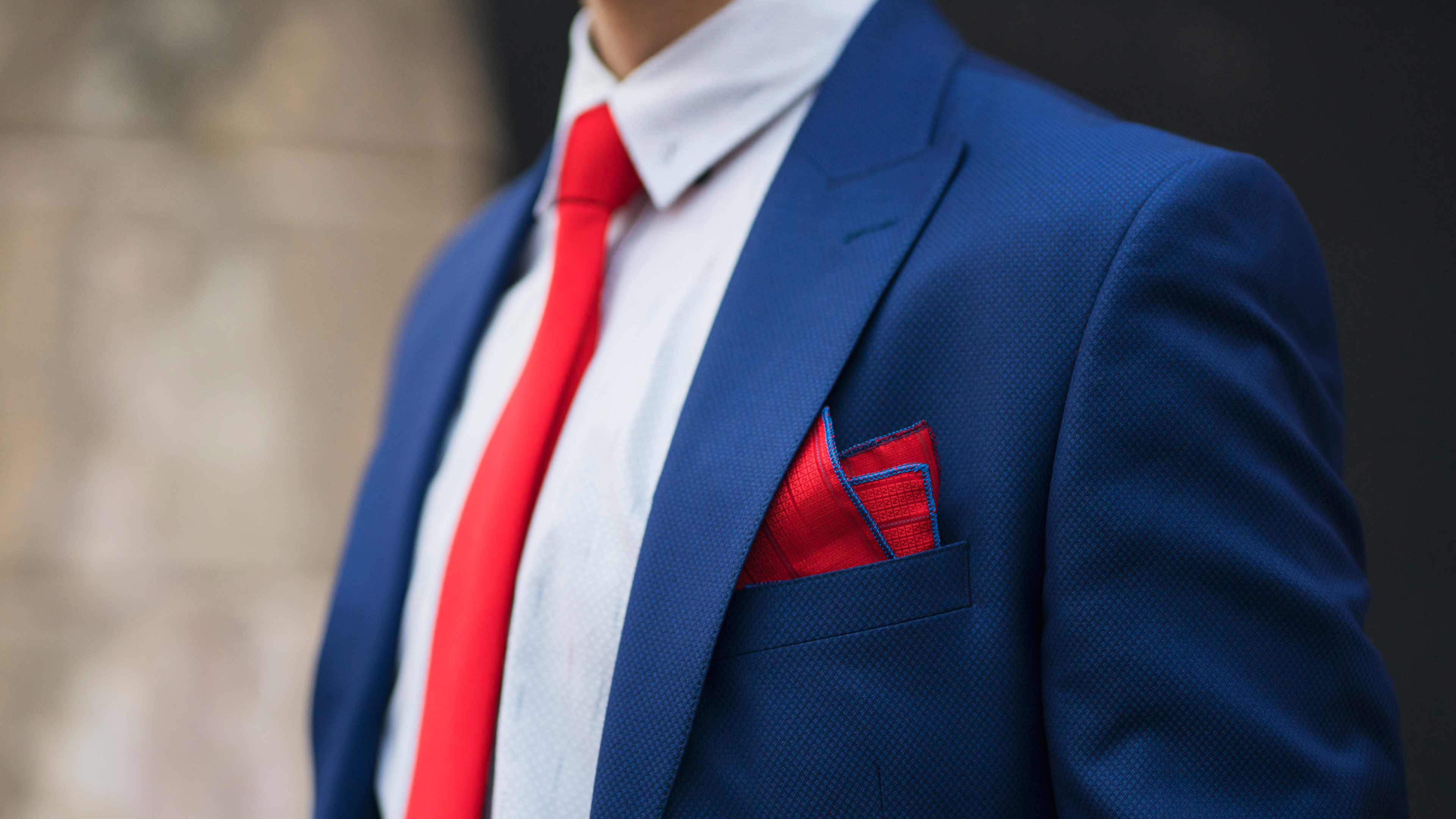 A close-up photo of an unrecognizable man in a blue blazer, white shirt, and a red tie.