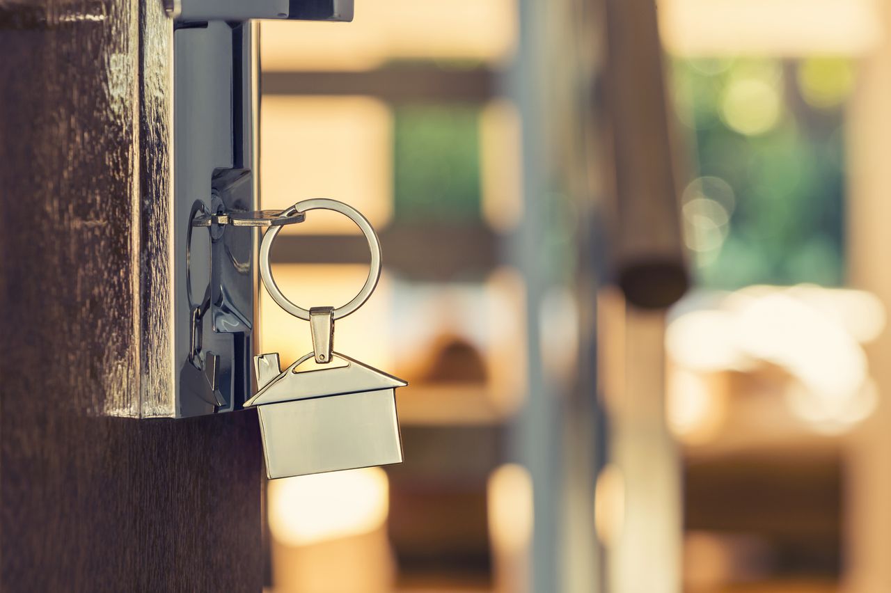 Opening a door with a key. Key is on a door lock. The keyring has a house shaped icon on the end and is shiny silver colour. 