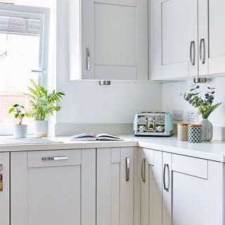 White painted kitchen and white cabinets with blue toaster and vases displayed on white worktop