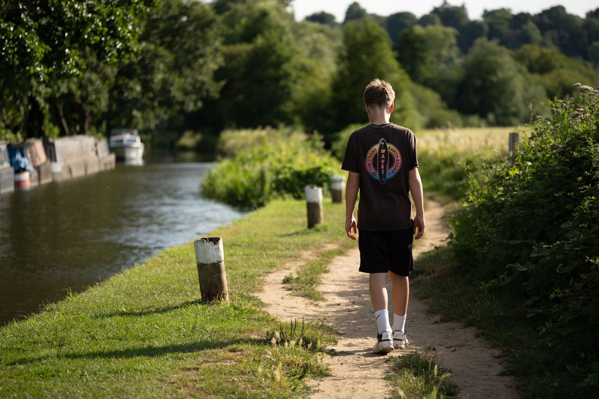 Viltrox AF 90mm F2.2 EVO lens image gallery: adolescent boy walking along a towpath, there are canal boats in the river, it's golden hour
