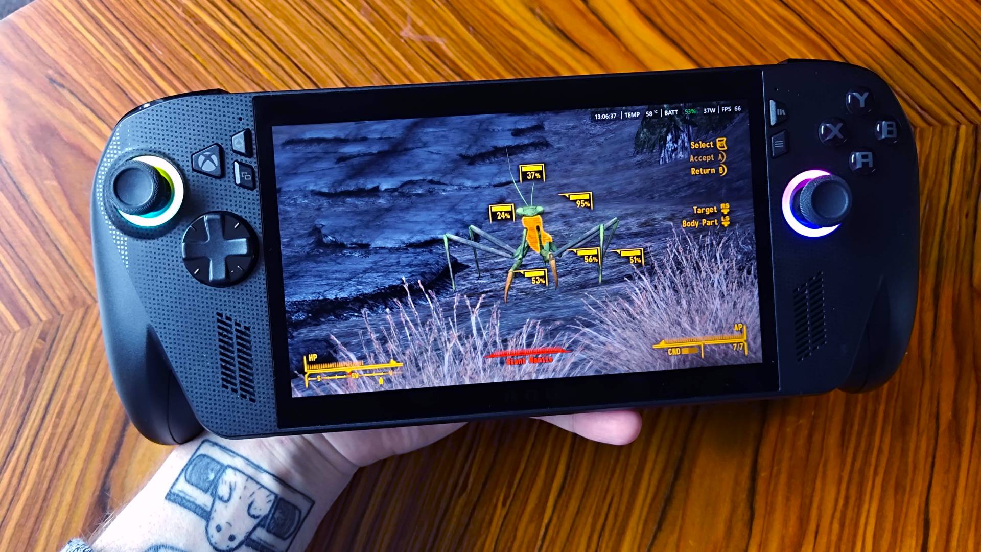 Hand holding ROG Xbox Ally X next to woodgrain table with Fallout New Vegas gameplay on screen featuring Mantis highlighted in VATS.