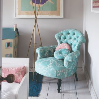 A dove-grey painted children's room with a patterned armchair in the corner and a doll house next to it