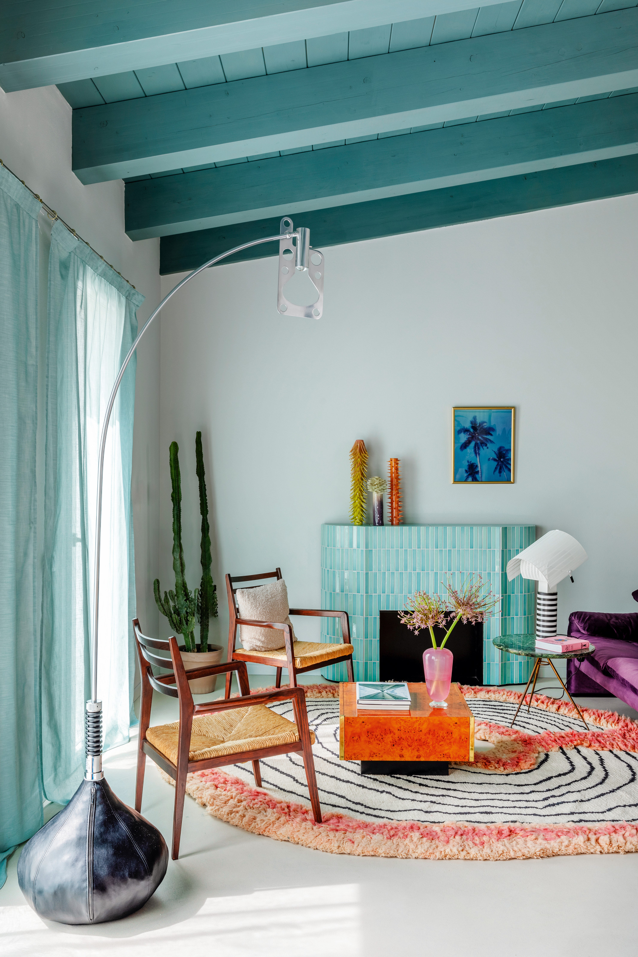 Living room with turquoise ceiling, turquoise tiled fireplace, circular rug and wooden armchairs with burl wood coffee table