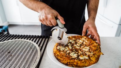 Person uses rotating blade to slice cooked pizza