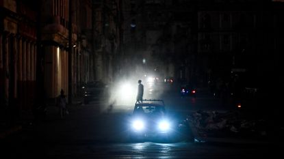 A man walks while cars cruise along a street during a blackout in Havana