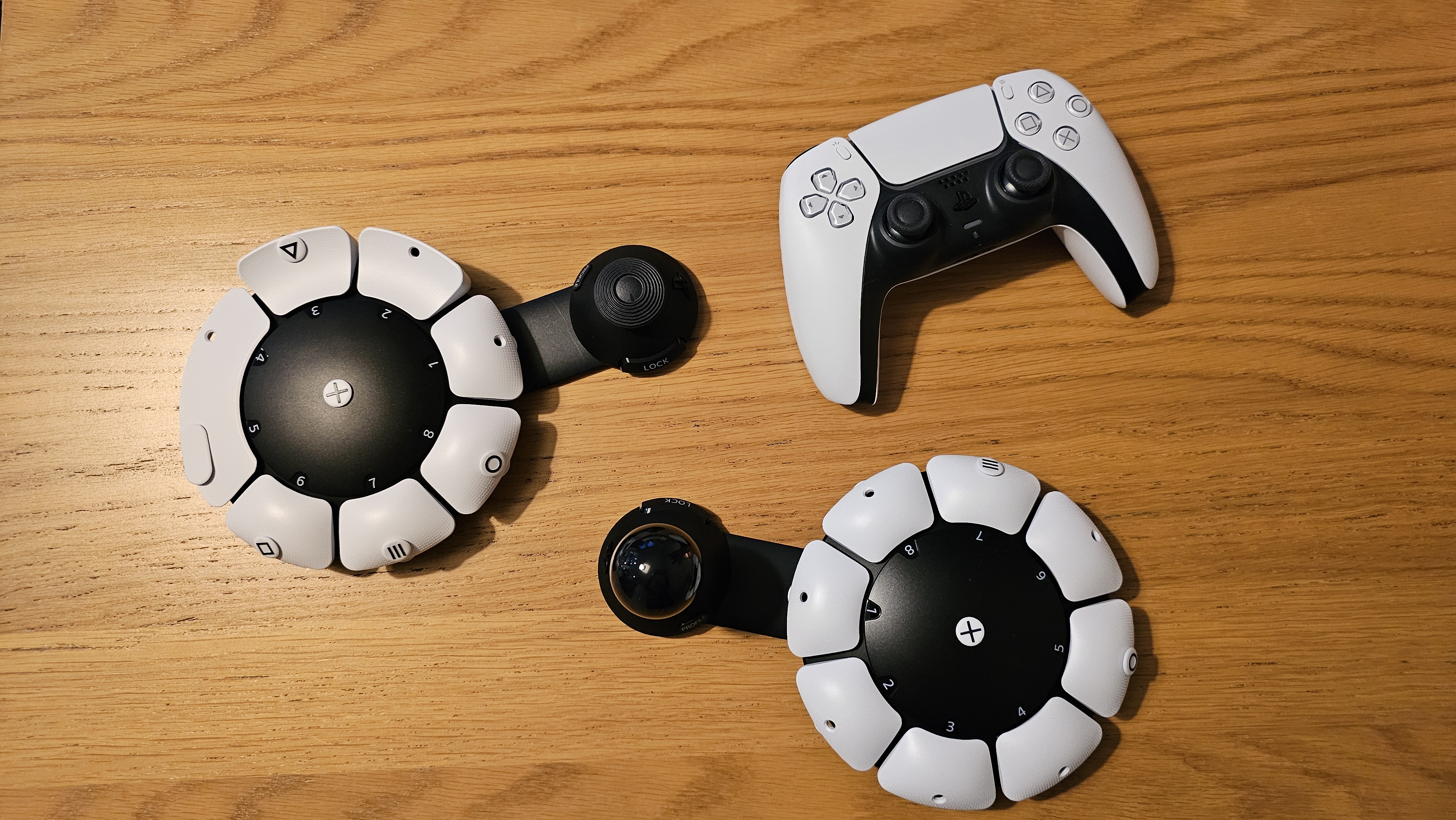 Two PlayStation Access controllers and a DualSense controller on a wooden surface
