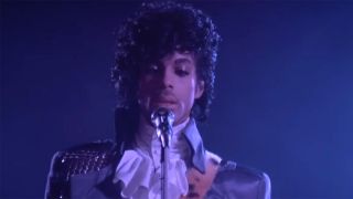 Prince performing in Frilly shirt and purple jacket in purple rain.