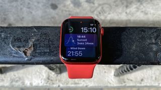 En röd Apple Watch 6 hänger över ett metallräcke och visar statistik och tiden på urtavlan.