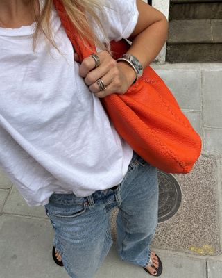 Woman wearing a white T-shirt, jeans, a red bag, and silver jewelry.