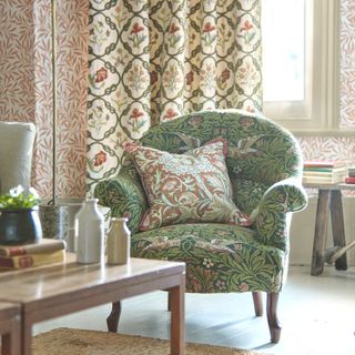 living room with green morris print chair and contrasting morris print cushion in red, red wallpaper and morris-style curtains