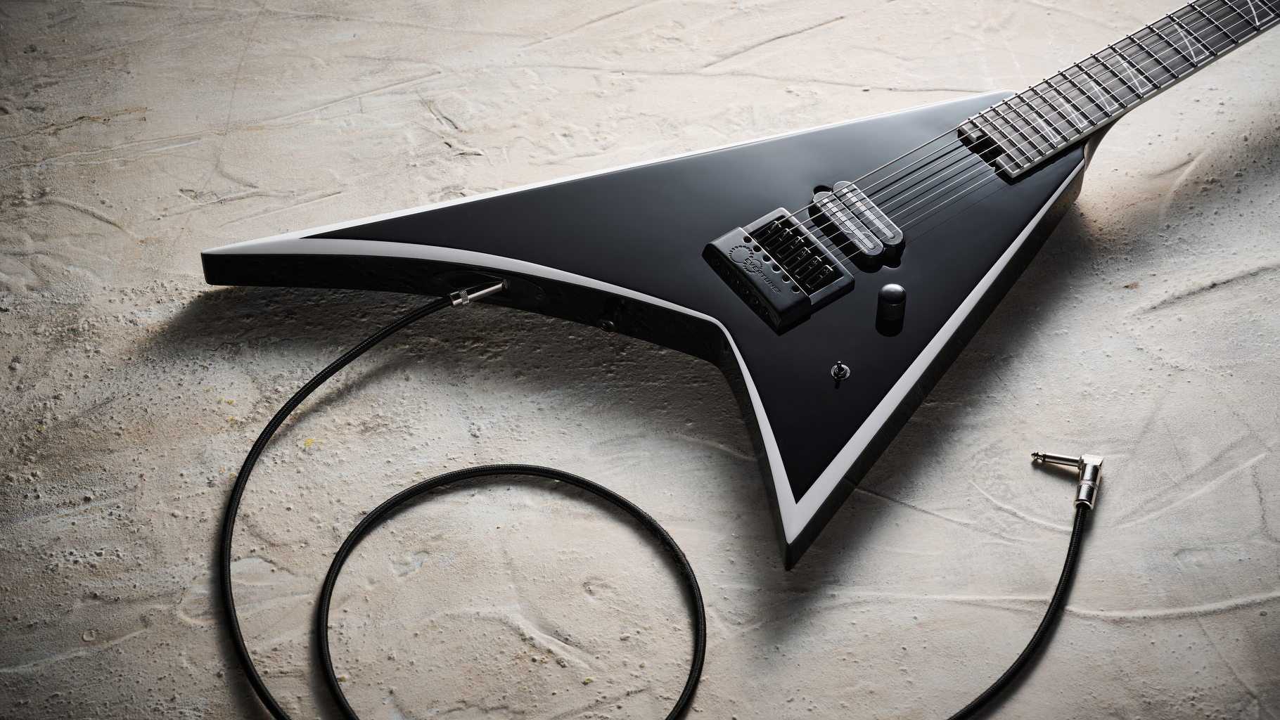 A Jackson Pro Plus Series Signature Christian Andreu Rhoads RR24 EVTN6 lying on a distressed white floor with a guitar cable plugged into it