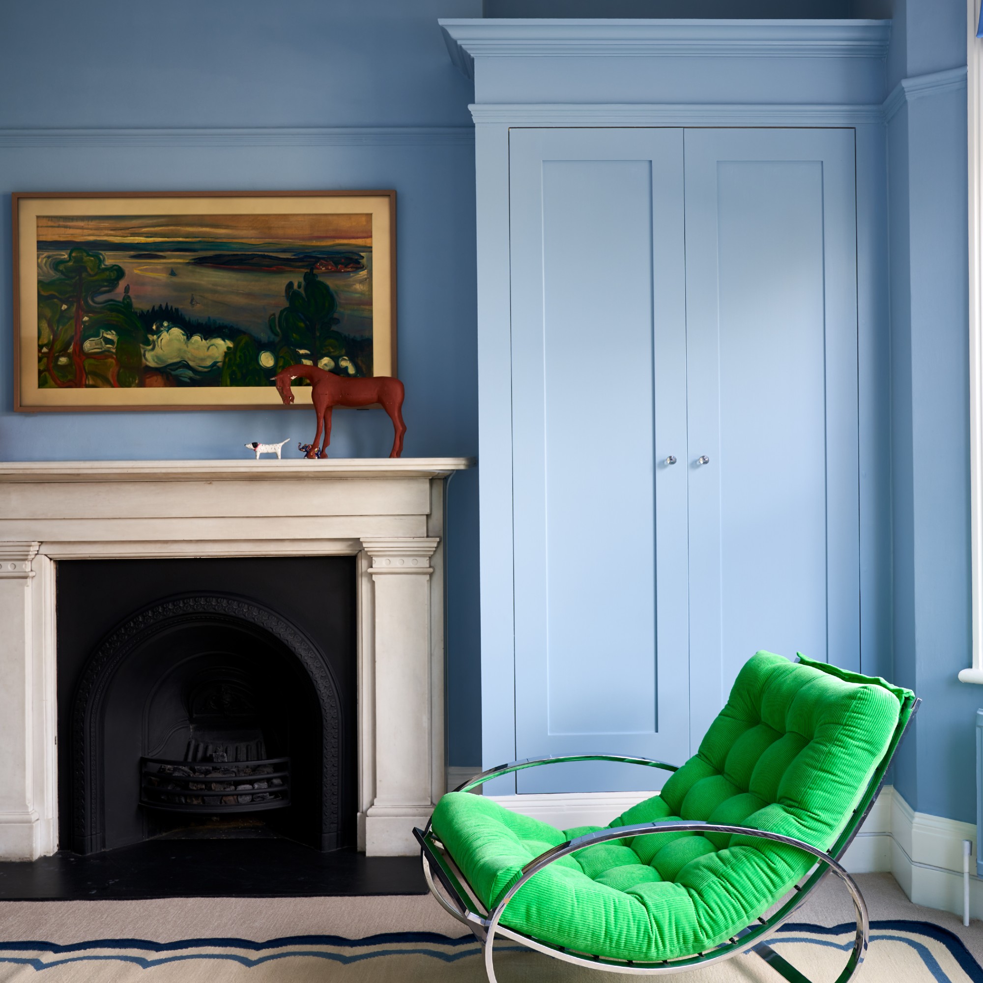 A room painted in Farrow &amp;amp; Ball's Lulworth Blue with a stone fireplace with apainting above it and a bright green lounge chair next to it