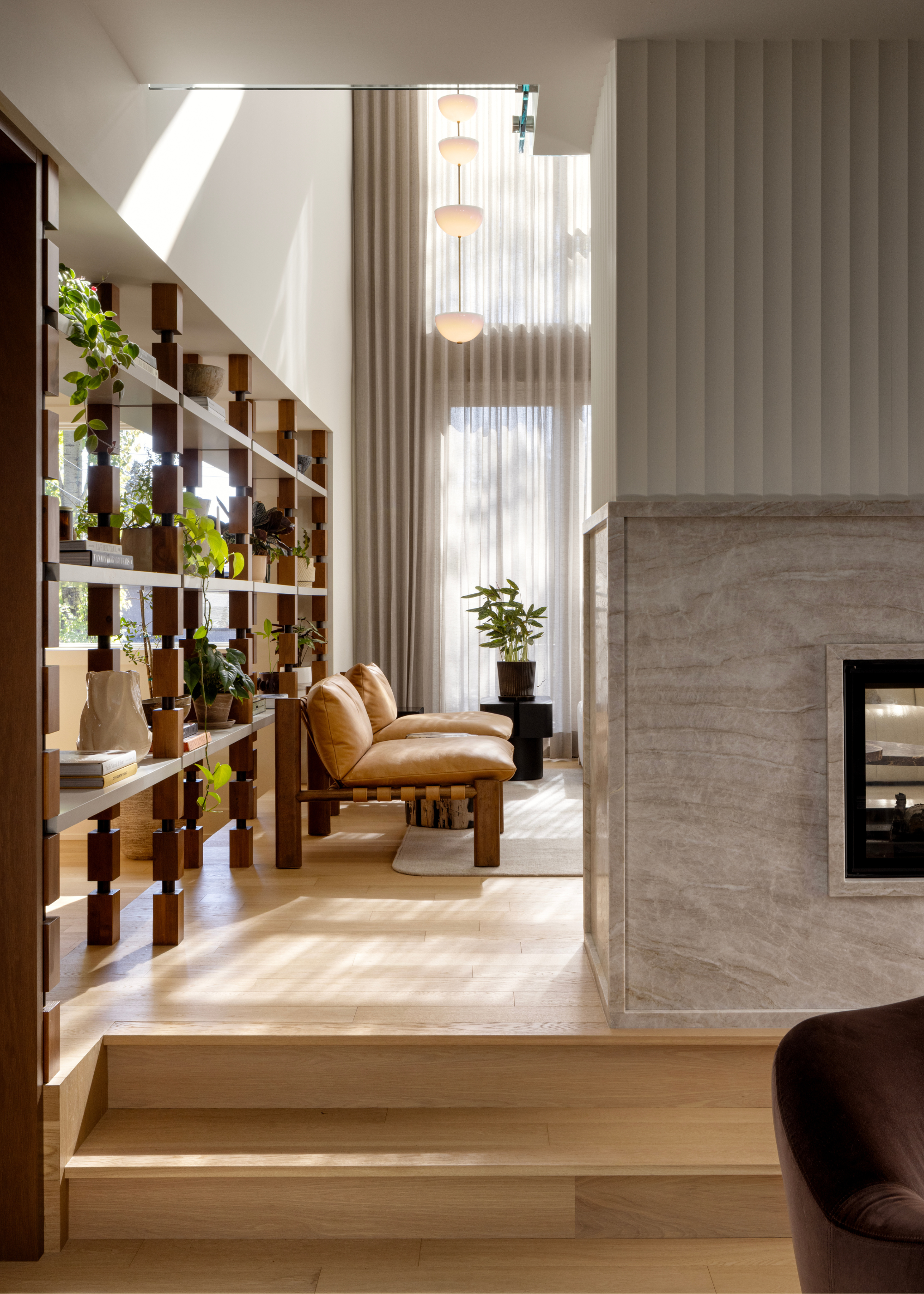 A living room with a fireplace, a pair of leather chairs, and a wall of open shelves with books and plants