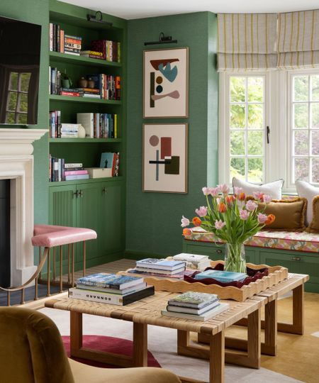 an emerald green english living room with bay window and window bench, wooden coffee table, fireplace, and bookshelves