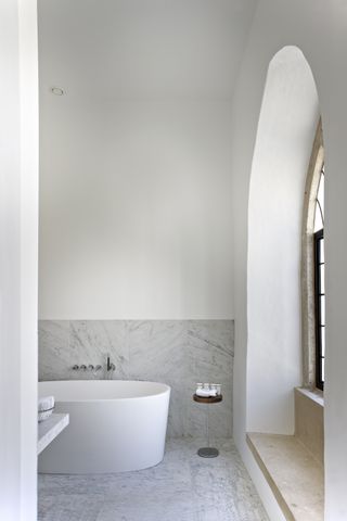 contemporary bathroom with white bath, marble floor tiles and some wall tiles, large chapel style window