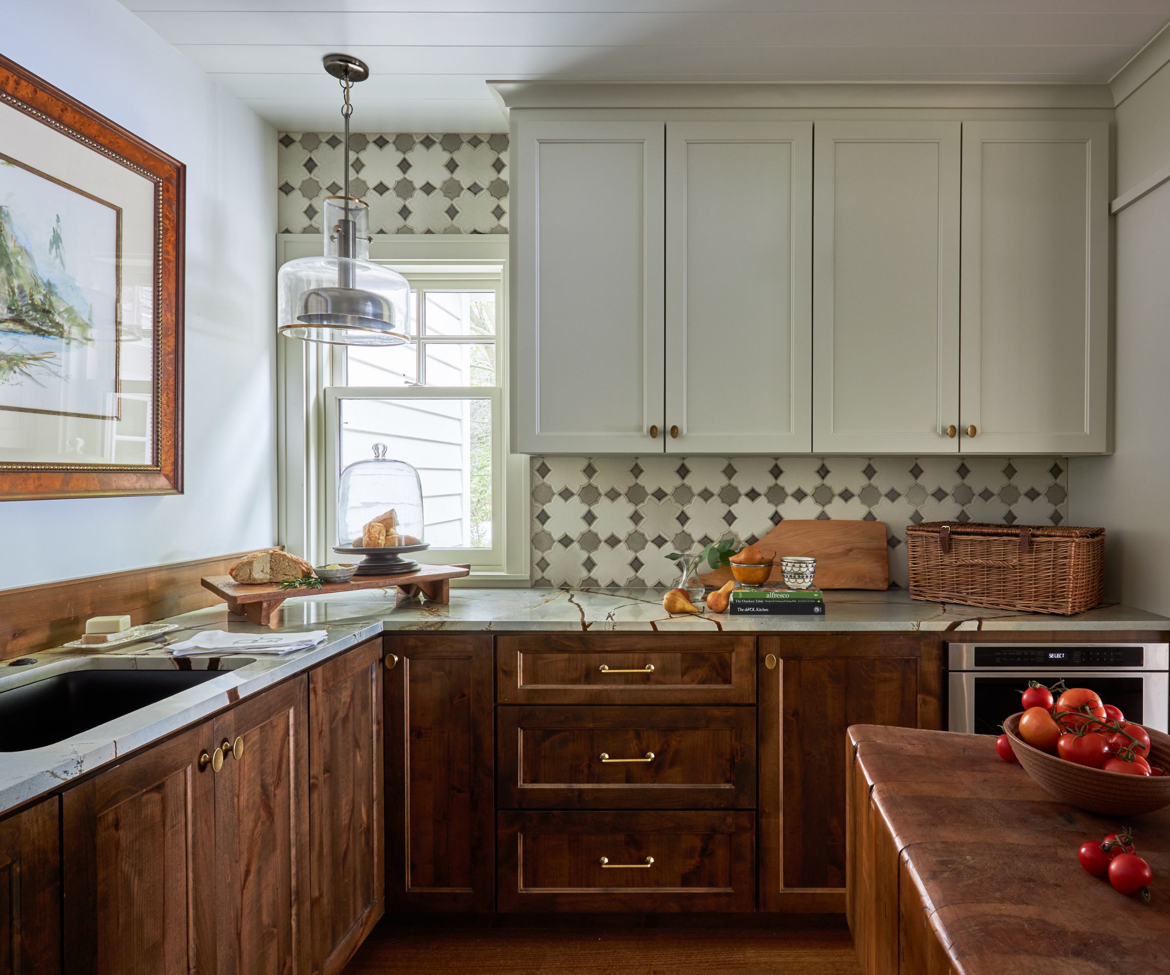 A cozy kitchen with wooden lower cabinets, white upper cabinets, marble countertops, and a selection of kitchenware as decor