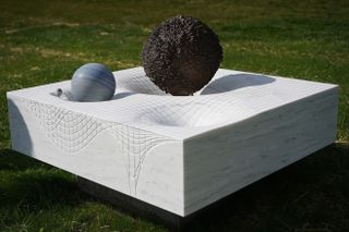 A view of a marble block sitting in the grass with four divots that represent space-time warps.