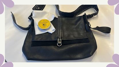 A shot of a black leather handbag on a table with a cloth and can of beeswax leather polish on top of it