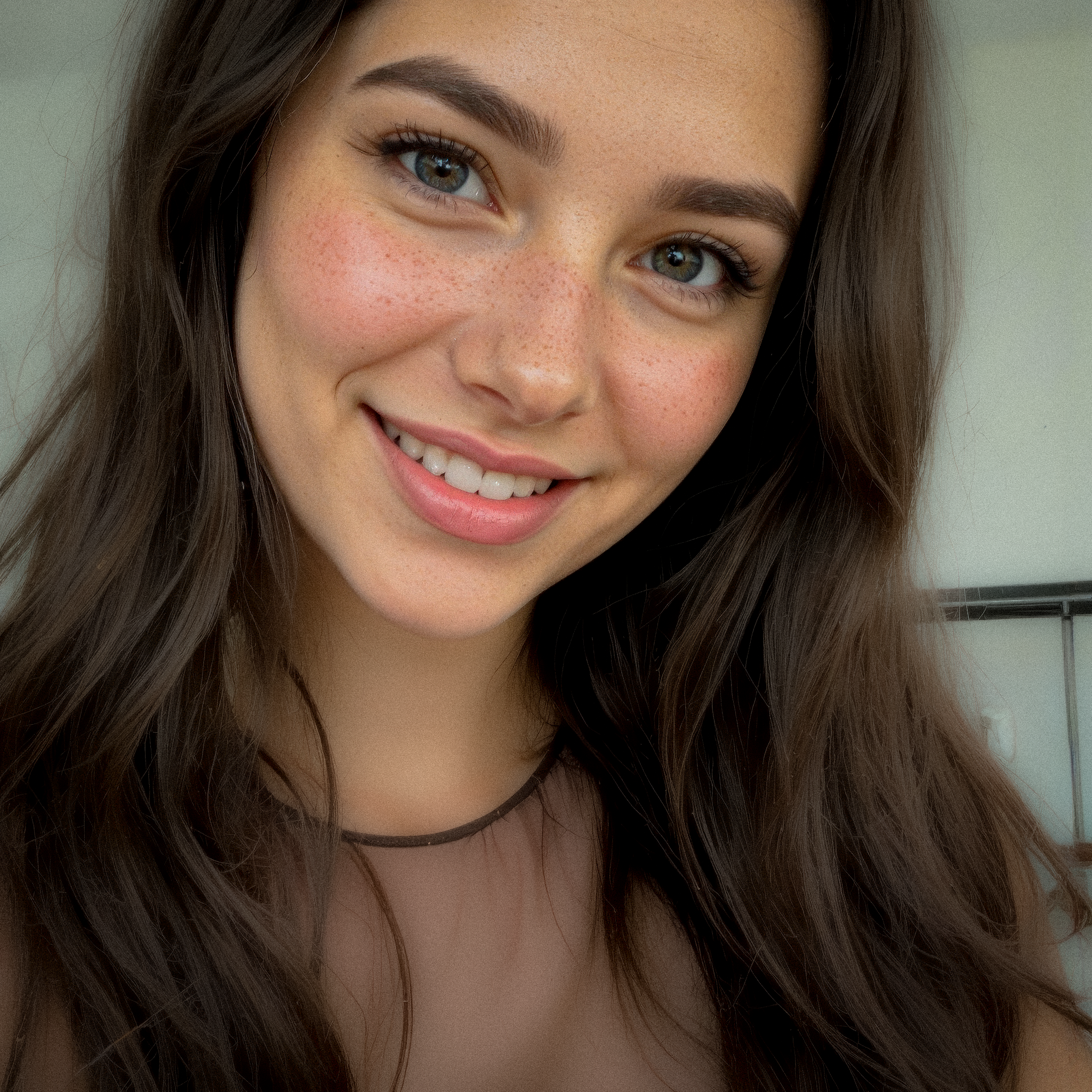 Close-up portrait of a smiling young woman with long dark hair, freckles, and natural makeup.