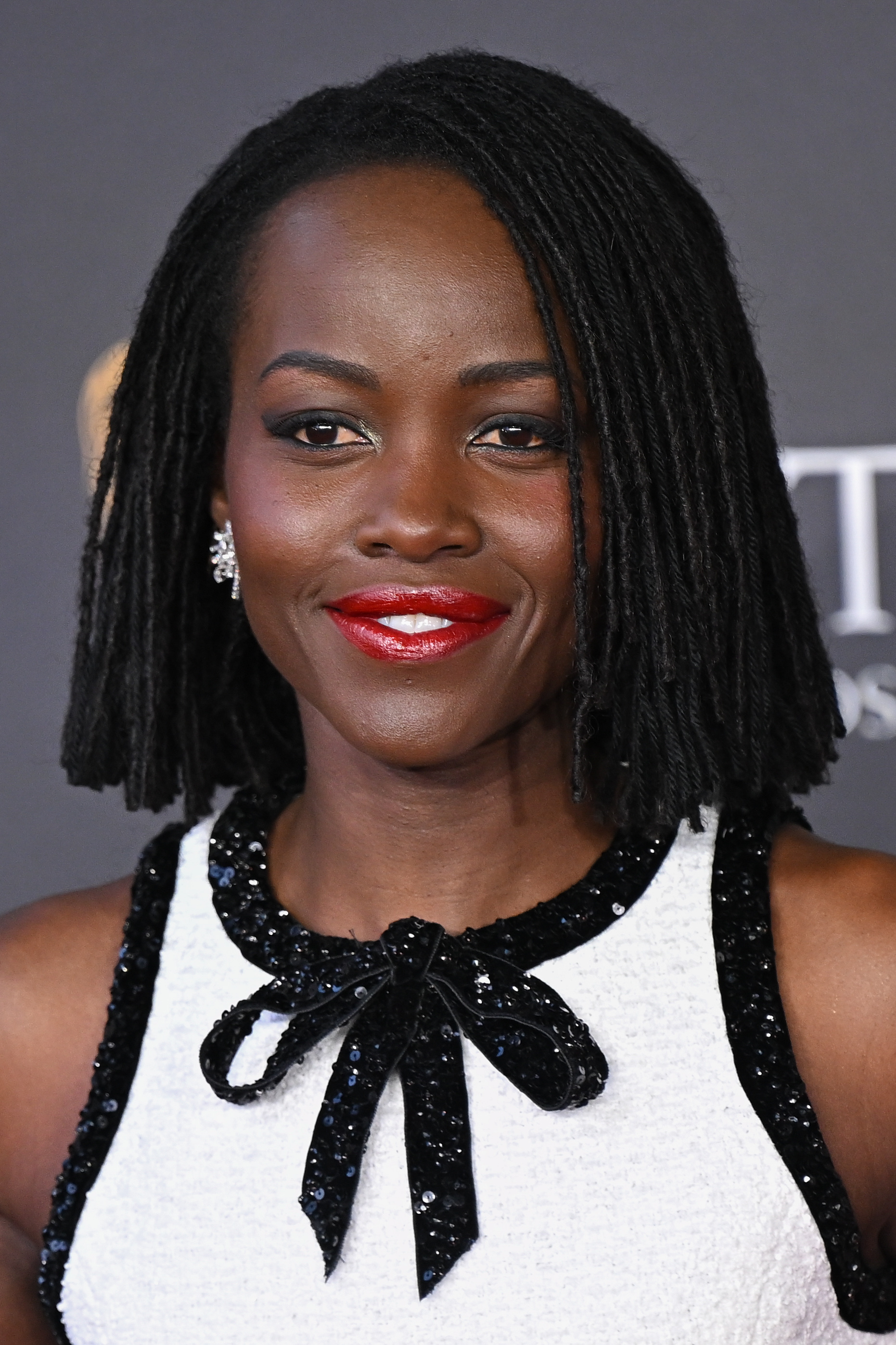 a black woman with a short loc hairstyle posing in front of a gray background