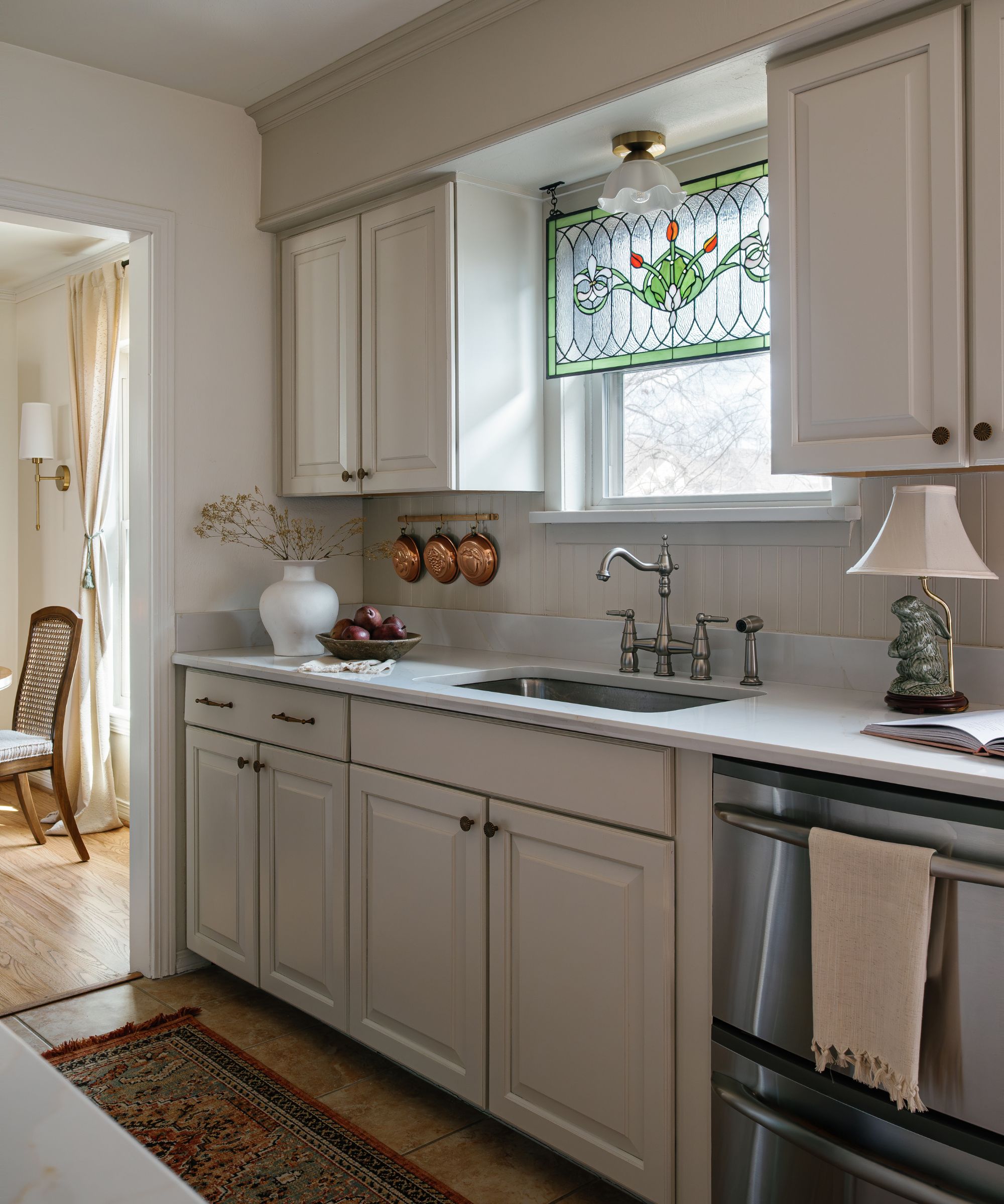 A small cream kitchen with a stained glass window feature and a brass pot hanger