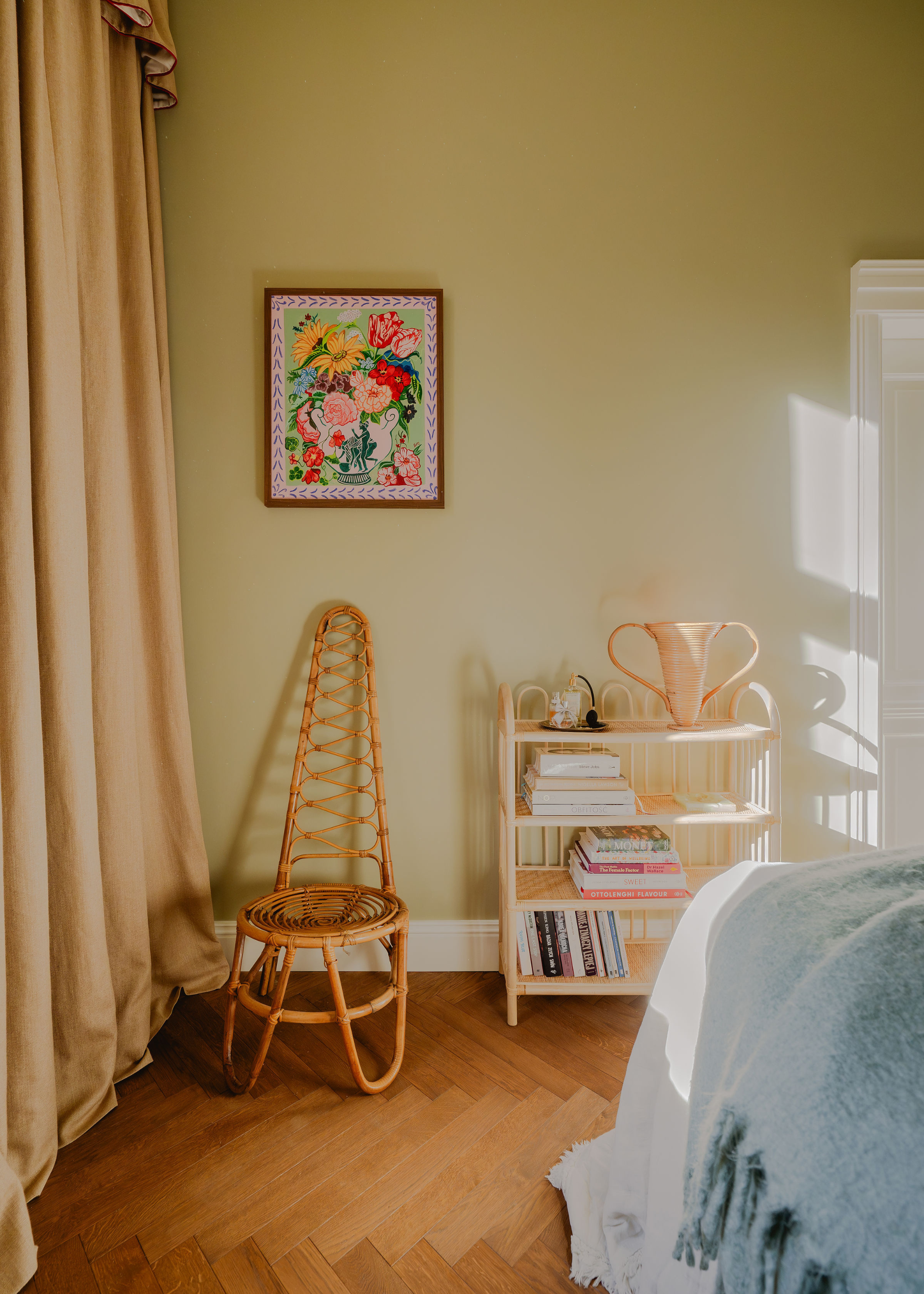 Green painted bedroom with colorful floral painting and a wicker chair in the corner