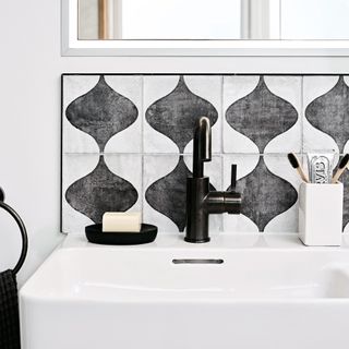 a close-up of a bathroom basin with a black and white patterned tile splashback and black taps