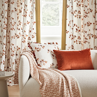 a plain sofa with a patterned throw and patterned curtains behind