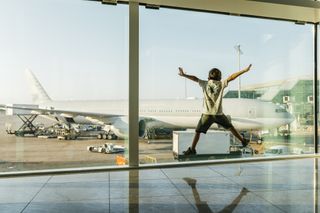 young child doing jumping jack while looking our of airport lounge window at a plane