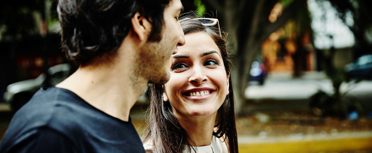 Defining the relationship- Smiling woman in discussion with boyfriend walking on sidewalk of city street on summer evening