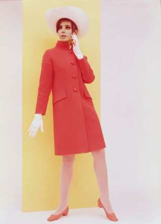 A woman modelling women's fashions in a studio portrait, wearing a red coat, with white wide-brimmed hat, white gloves and red shoes, 1966. (Photo by Archive Photos/Getty Images).