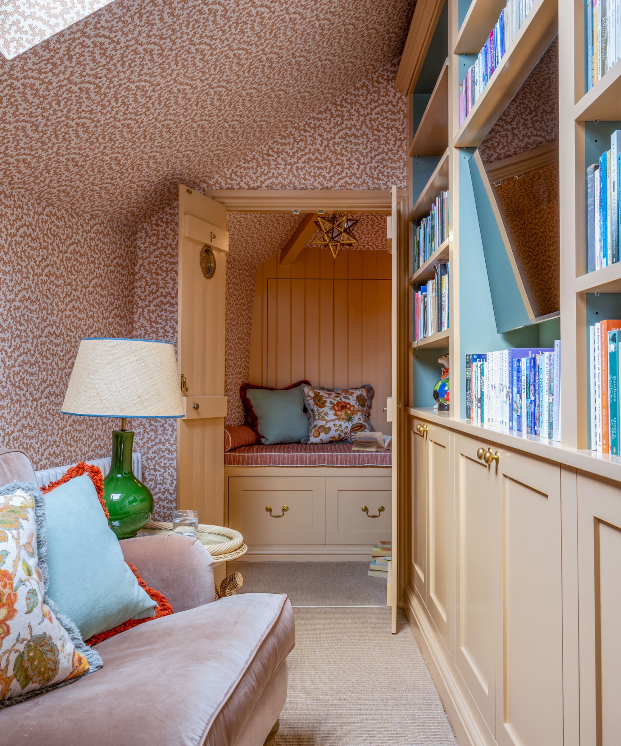 an attic room pattern drenched in pink squiggly wallpaper with custom cabinetry and bookshelves painted yellow, a styled couch, a doors leading into a cozy yellow reading nook