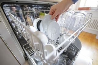 Hand reaching for clean dishes in dishwasher