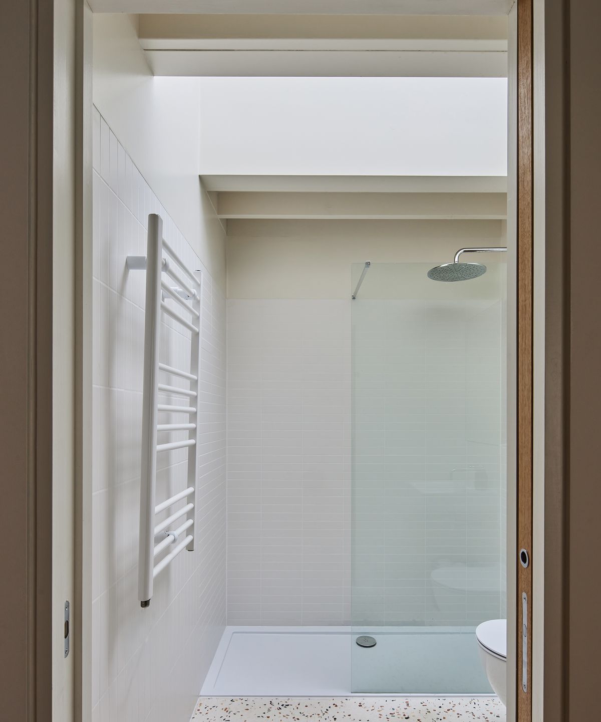 A small bathroom with terrazzo floor tiles and walk-in shower and ceiling light to allow plenty of natural light in